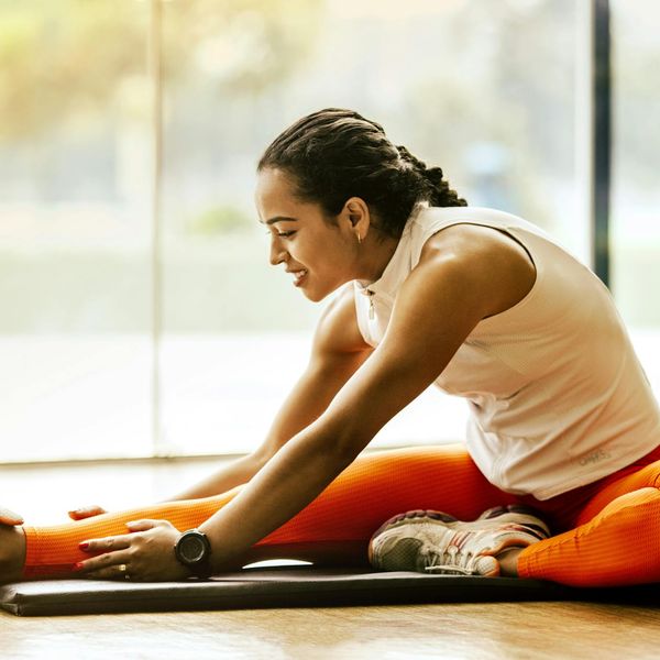 Smiling woman stretching gently on a yoga mat in a bright space.