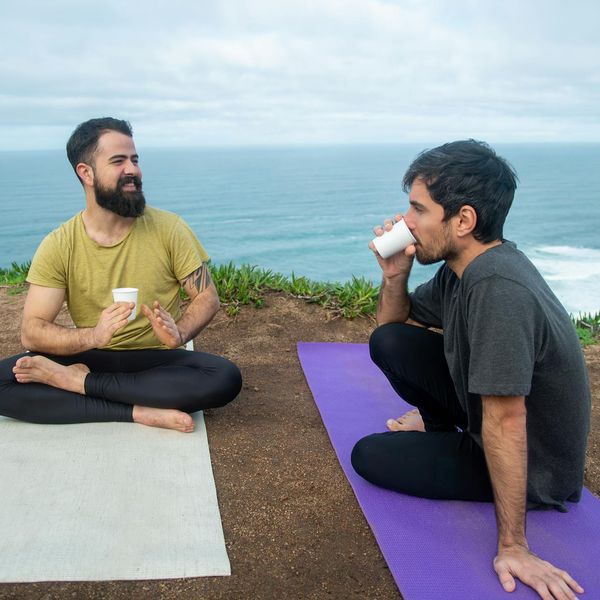 Woman sitting peacefully with a cup of tea near a yoga mat.